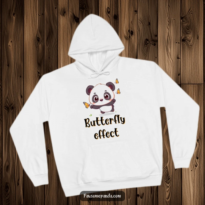 Funny kawaii panda cub with big, surprised eyes, chasing a butterfly, featured on a cozy hoodie, radiating innocence.